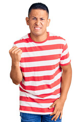 Wall Mural - Young handsome latin man wearing casual clothes angry and mad raising fist frustrated and furious while shouting with anger. rage and aggressive concept.