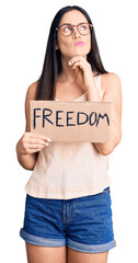 Poster - Young beautiful caucasian woman holding freedom banner serious face thinking about question with hand on chin, thoughtful about confusing idea