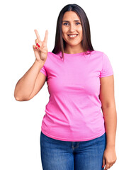 Canvas Print - Young beautiful brunette woman wearing casual t-shirt smiling with happy face winking at the camera doing victory sign. number two.