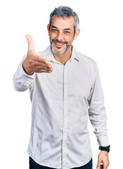 Canvas Print - Middle age hispanic with grey hair wearing casual white shirt smiling friendly offering handshake as greeting and welcoming. successful business.