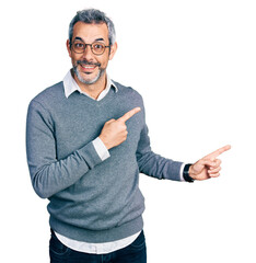 Canvas Print - Middle age hispanic with grey hair wearing glasses smiling and looking at the camera pointing with two hands and fingers to the side.