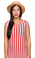 Poster - Young hispanic woman wearing summer hat with serious expression on face. simple and natural looking at the camera.