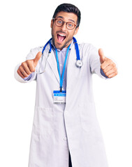 Wall Mural - Young hispanic man wearing doctor uniform and stethoscope approving doing positive gesture with hand, thumbs up smiling and happy for success. winner gesture.