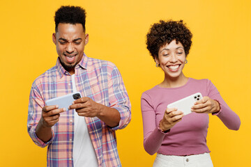 Poster - Young couple two friends family man woman wearing casual clothes together use play racing app on mobile cell phone hold gadget smartphone for pc video games isolated on plain yellow orange background.