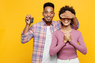 Young smiling couple two friend family man woman of African American ethnicity wear purple casual clothes together hold car key fob keyless system cover eyes isolated on plain yellow orange background