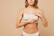 © ViDi Studio - Close up cropped young nice lady woman with slim body perfect skin wearing nude top bra lingerie stand holding put hand on breast isolated on plain light beige background. Lifestyle diet fit concept.