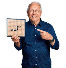 Poster - Senior man with grey hair holding asian go game board smiling happy pointing with hand and finger