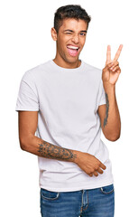 Sticker - Young handsome african american man wearing casual white tshirt smiling with happy face winking at the camera doing victory sign. number two.