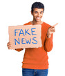 © Krakenimages.com - Young african amercian man holding fake news banner smiling happy pointing with hand and finger to the side