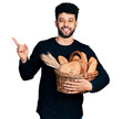 © Krakenimages.com - Young arab man with beard holding wicker basket with bread smiling happy pointing with hand and finger to the side
