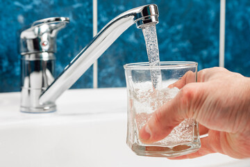 Hand holding a glass of water poured from a water tap