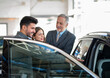 © Minerva Studio - Young family talking to the salesman and choosing their new car in a showroom