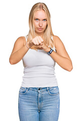 Poster - Young blonde girl wearing casual style with sleeveless shirt punching fist to fight, aggressive and angry attack, threat and violence