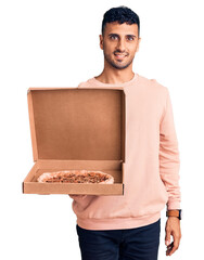 Poster - Young hispanic man holding delivery pizza box looking positive and happy standing and smiling with a confident smile showing teeth