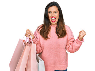 Sticker - Beautiful hispanic woman holding shopping bags screaming proud, celebrating victory and success very excited with raised arms