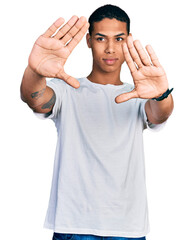 Young hispanic man wearing casual white t shirt doing frame using hands palms and fingers, camera perspective