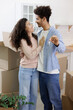© MyJuly - moving to new apartment relocation. happy couple, African American man and woman, hold keys in hands and collect personal belongings in cardboard boxes. purchase of new housing, mortgage.