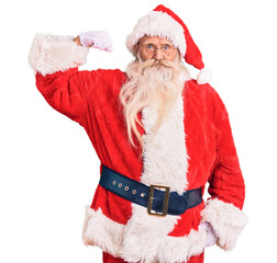 Old senior man with grey hair and long beard wearing traditional santa claus costume strong person showing arm muscle, confident and proud of power