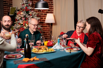 Wall Mural - Diverse persons gathering around table to celebrate festive seasonal holiday, feeling cheerful during christmas eve dinner. Friends and family enjoying event at home with traditional homemade meal.