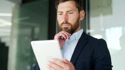 Businessman in formal suit is using digital tablet standing in business office. Worker reads or typing message, chats with a client, banking in app, checks email or swiping browsing online. Close up