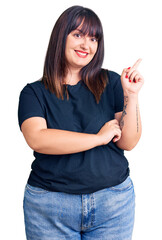 Canvas Print - Young plus size woman wearing casual clothes with a big smile on face, pointing with hand and finger to the side looking at the camera.