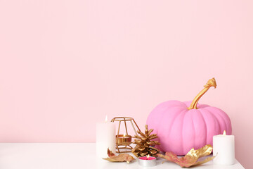 Wall Mural - Pink painted pumpkin with autumn leaves and burning candles on white table near color wall