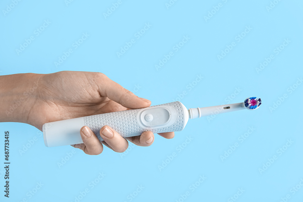 Female hand with electric toothbrush on blue background.