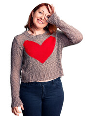 Canvas Print - Young beautiful redhead woman wearing casual heart sweater smiling happy doing ok sign with hand on eye looking through fingers