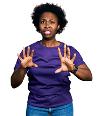 Canvas Print - African american woman with afro hair wearing casual purple t shirt afraid and terrified with fear expression stop gesture with hands, shouting in shock. panic concept.