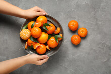Woman Holding Plate With Sweet Mandarins And Leaves On Grey Background