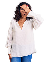 Canvas Print - Middle age beautiful woman wearing casual sweater peeking in shock covering face and eyes with hand, looking through fingers with embarrassed expression.