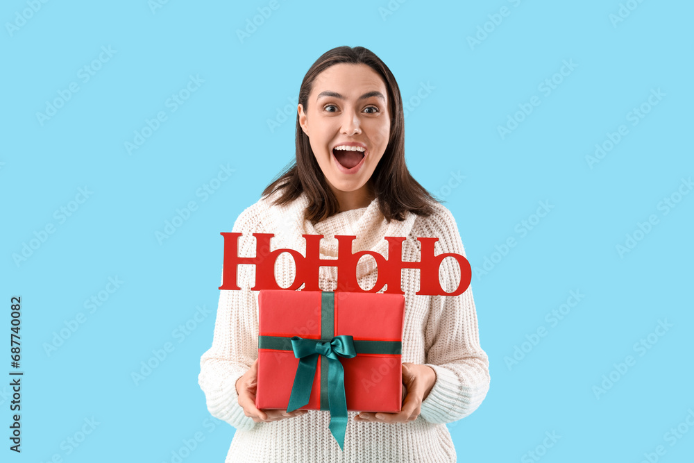 Young woman with Christmas greeting and present on blue background