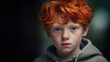Studio portrait of a young boy with bright red hair, wearing a grey hoodie. He is staring directly into the viewer, capturing their attention.