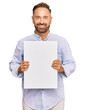 © Krakenimages.com - Handsome middle age man holding blank empty banner looking positive and happy standing and smiling with a confident smile showing teeth