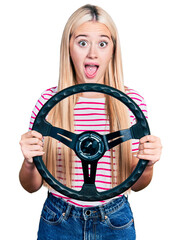 Wall Mural - Beautiful blonde woman holding steering wheel celebrating crazy and amazed for success with open eyes screaming excited.