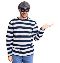 Canvas Print - Young handsome man wearing burglar mask smiling cheerful presenting and pointing with palm of hand looking at the camera.