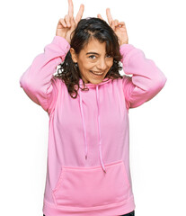 Wall Mural - Young hispanic woman wearing casual sweatshirt posing funny and crazy with fingers on head as bunny ears, smiling cheerful