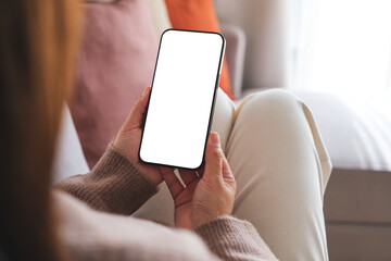 Wall Mural - mockup image of a woman holding mobile phone with blank desktop white screen while sitting on a sofa