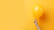 Hand holding an inflated yellow balloon with yellow background, space for text
