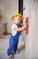 Wall Mural - Child construction worker checking wall surface with spirit level tool. Full length of kid in work overalls using level instrument while preparing wall for repair work at home during renovation.