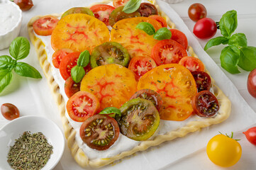 Wall Mural - Raw tomatoes pie or galette from puff pastry and cheese filling on a white wooden background. Vegetarian healthy food. Selective focus.