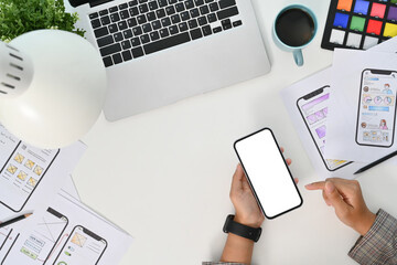 Young creative woman using mobile phone at desk with paper sketches for mobile interface