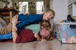 © Halfpoint - Portrait of father embracing his two sons at home, having fun, lying on floor and laughing.