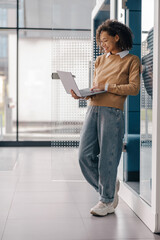 Wall Mural - Stylish business woman using laptop while standing on modern office background