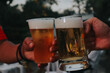 © ผดุงศักดิ์ กิจมานะทร - two hands holding frosty mugs of beer, one full and one half-empty, during what appears to be a social event.