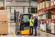 © Halfpoint - Female forklift driver, warehouse worker talking with manager, standing by forklift. Warehouse worker preparing products for shipmennt, delivery, checking stock in warehouse.
