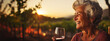 Senior smiling woman with a glass of wine, blurred backdrop of vineyard on a sunset. Generative AI