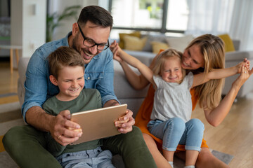 Wall Mural - Happy young family having fun time at home. Parents with children using tablet