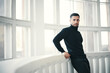 © GVS - Handsome young man in black turtleneck leans on balcony railings, with large windows in the backgroun