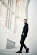 © GVS - Handsome fashionable man model in an all-black clothing outfit posing on white staircase